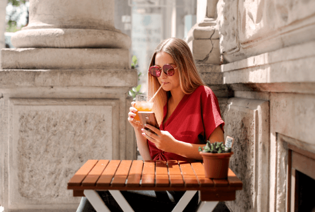 Casual woman texting sample text messages to customers and drinking coffee