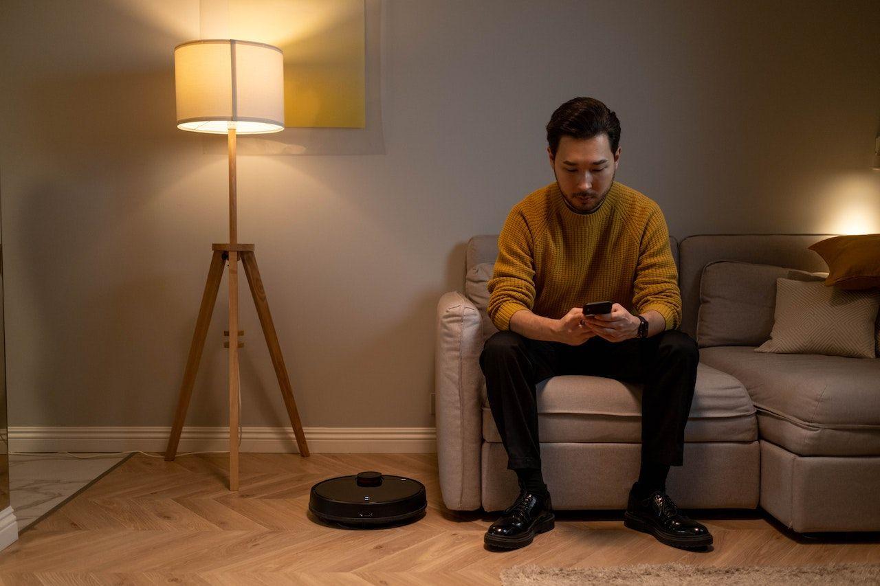 Man texting in dimly lit room with Roomba vacuum cleaner